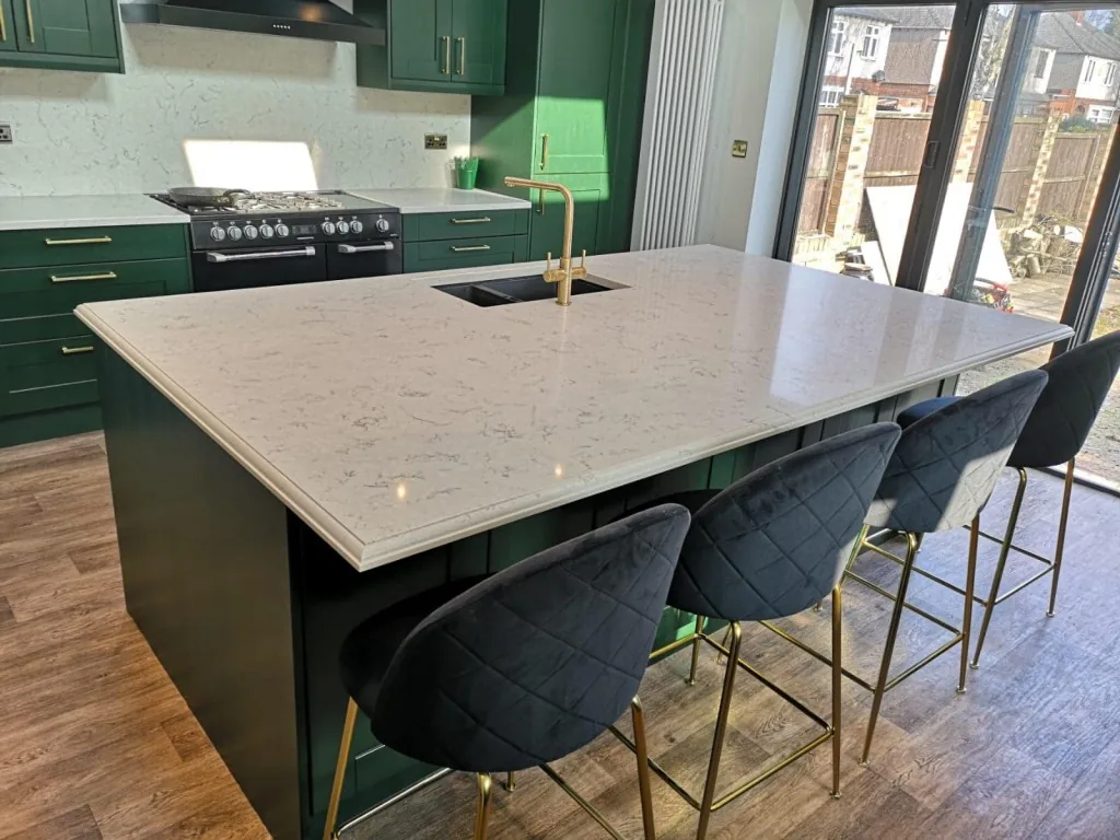 Deep green painted Shaker kitchen with large stone island and brass bar stools